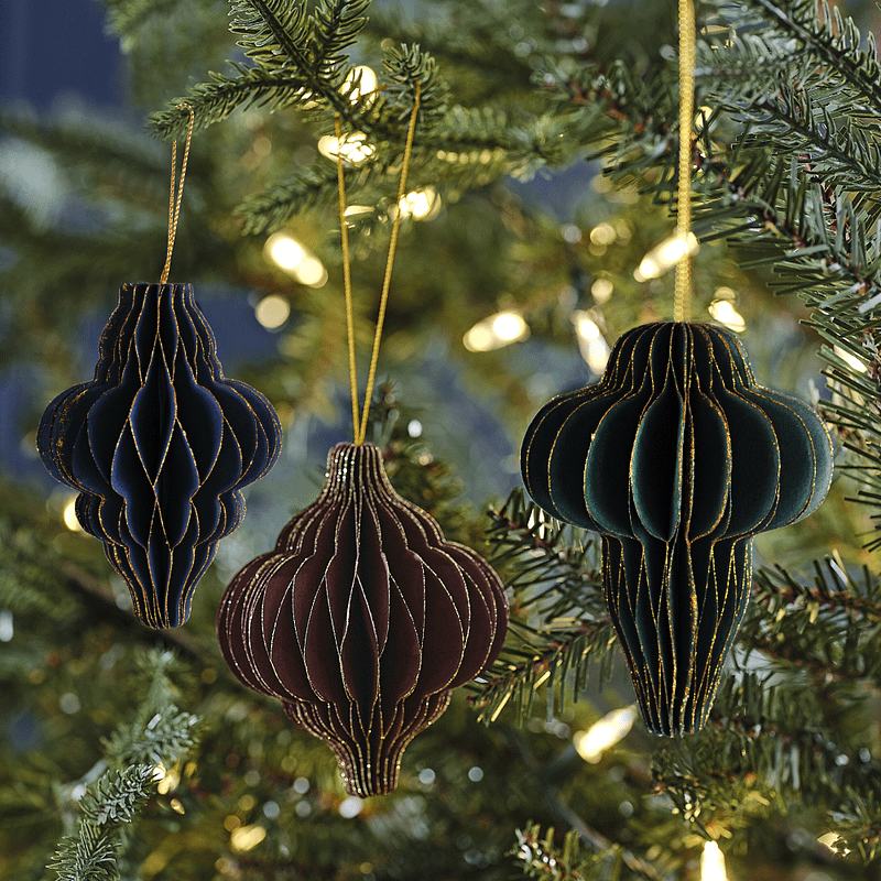 Honeycomb hangers met gouden glitterrandin de kleuren marinablauw, donkerrood en donkergroen hangen in de kerstboom versierd met een lichtjesslinger