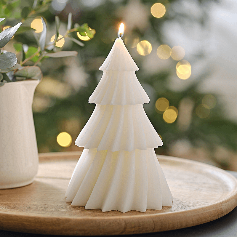 Kaars in de vorm van een witte kerstboom staat op een houten plateau voor een kerstboom met lampjes