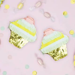 Pinata in de vorm van een cupcake in de kleuren goud, geel, lichtroze en lichtgroen op een roze achtergrond omringd met snoepjes