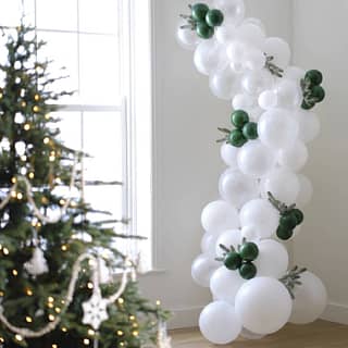 Ballonnenboog met witte en groene ballonnen en hulsttakjes naast kerstboom