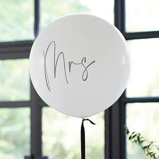 Witte ballon met de zwarte tekst 'Mrs' zweeft voor een raam met zwarte kozijnen