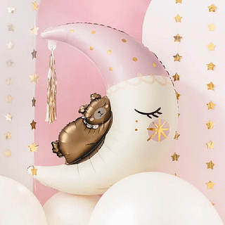 Folieballon in de vorm van een halve maan met een bruin beertje erop zweeft in een roze kamer met gouden sterrenslingers