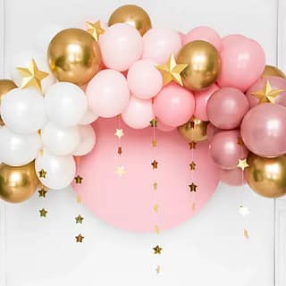 Ballonnenboog van roze gouden zilveren en witte ballonnen met daarachter een wolk en gouden sterren slingers