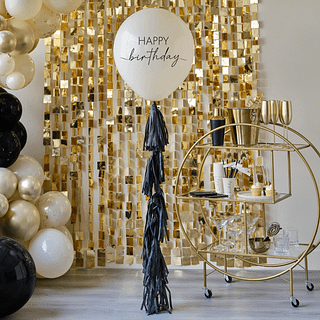 Grote ballon met zwarte tekst happy birthday en zwarte tasselslinger hangt voor een gouden cocktailkarretje