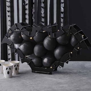 Ballonstandaard in de vorm van een vleermuis met zwarte ballonnen en lampjes op een tafel met spookjes bekers