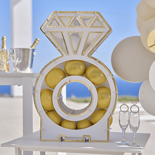 Ballonstandaard in de vorm van een ring met gouden en witte ballonnen staat op een tafel voor een blauwe zee