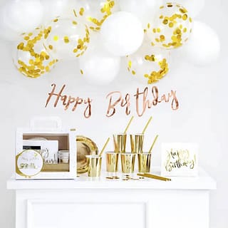 Tafel met feestversiering zoals gouden bekers servetten met daarboven een happy birthday slinger en ballonnen