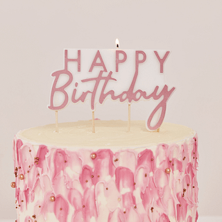 Rosé gouden kaars met de tekst 'Happy birthday' staat op een roze taart