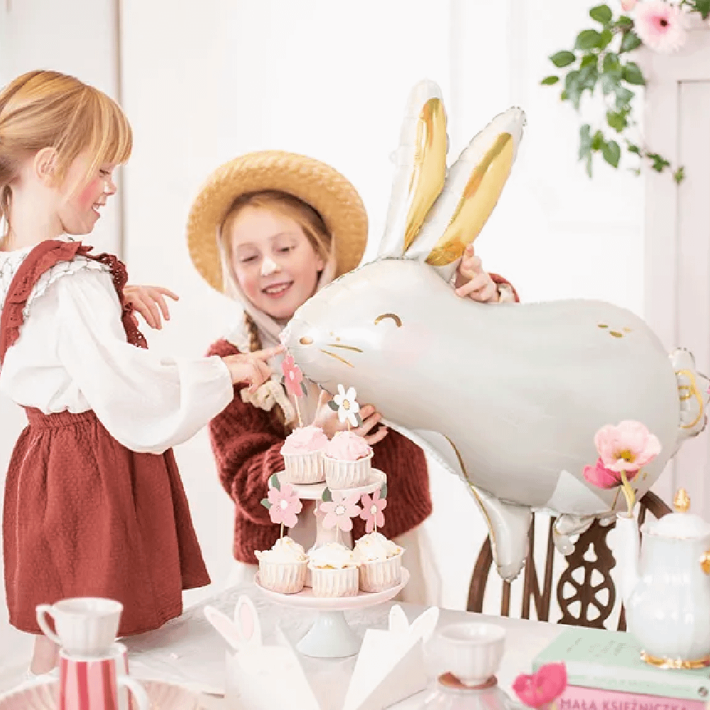 Twee meisjes hebben een folieballon in de vorm van een haas en zitten voor een tafel met roze versiering en mokken
