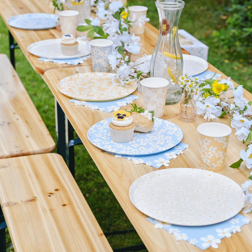 Pastelkleurige bordjes met bloemenprint staan op een houten tafel met cupcakes en planten