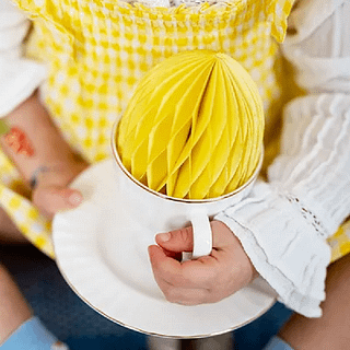 Gele honeycomb zit in een wit schoteltje en wordt vastgehouden door een meisje met een geel jurkje en witte blouse