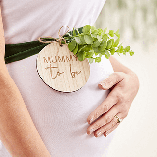 Zwangere vrouw met buiksjerp van groen fluweel en een houten rondje met de tekst 'Mummy to be'