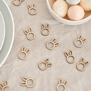 Houten confetti in de vorm van konijntjes op een bruin tafelkleed naast een schaal met eieren