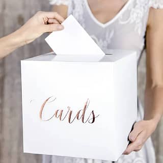 Vrouw houdt witte kaartendoos vast met rosé gouden letters erop en iemand doet er een envelop in